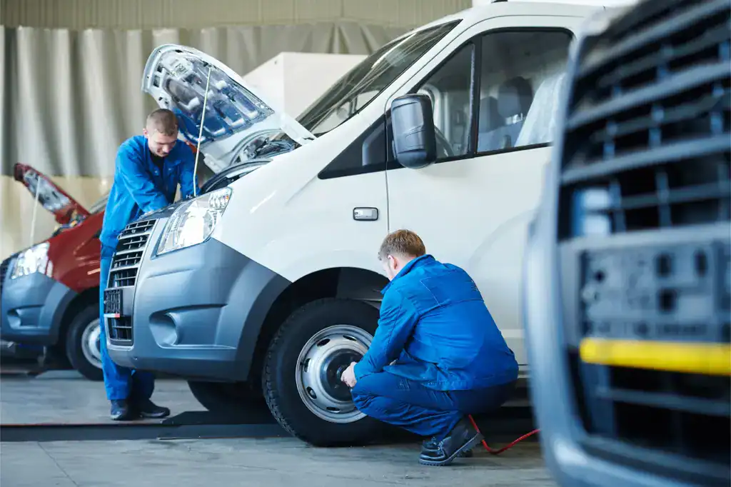 Technicians repair a commercial delivery van in a fleet maintenance garage.